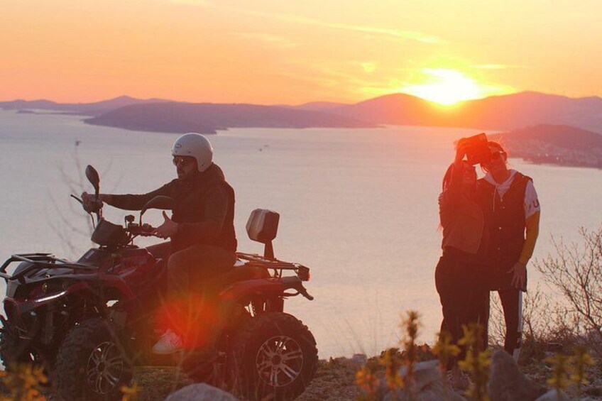 A sunset over a body of water with mountains in the background and a person on an ATV. 4
