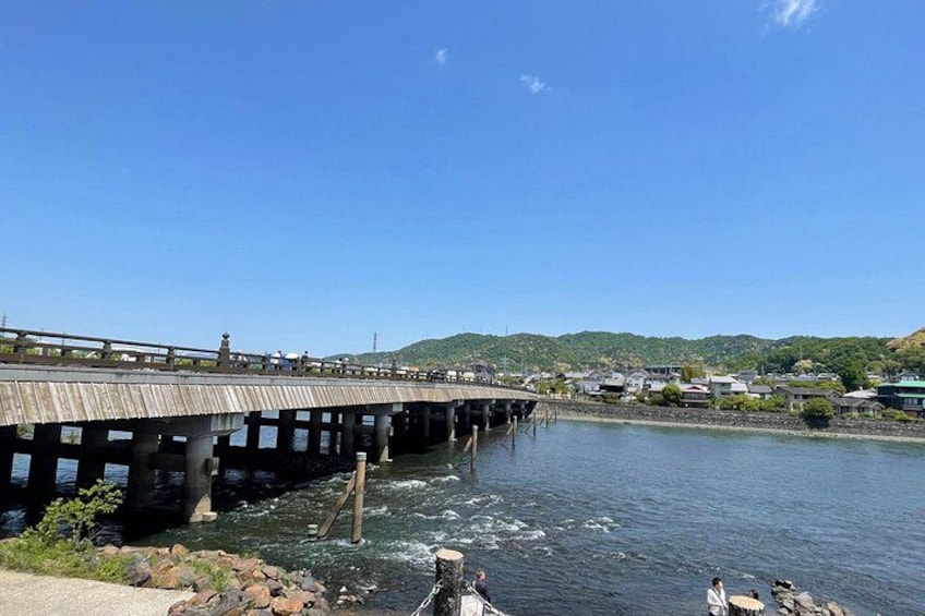 A wooden bridge over a river, with houses and hills in the background. 2