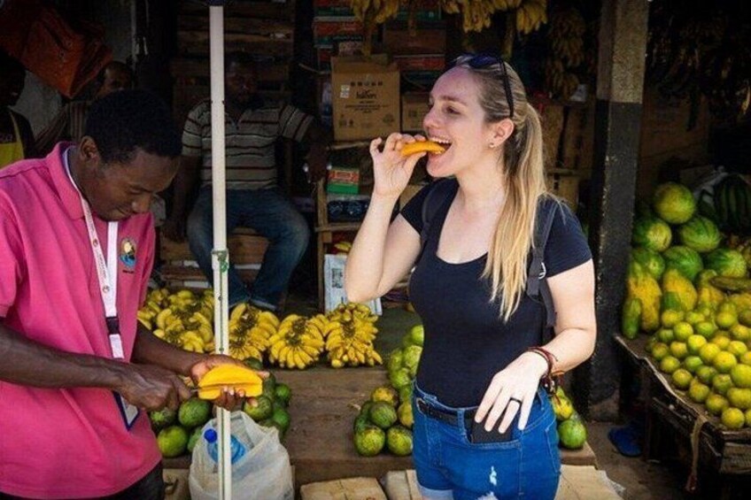 Una persona pesa delle banane a una bancarella di mercato, sullo sfondo si vedono diversi tipi di frutta e scatole. 2