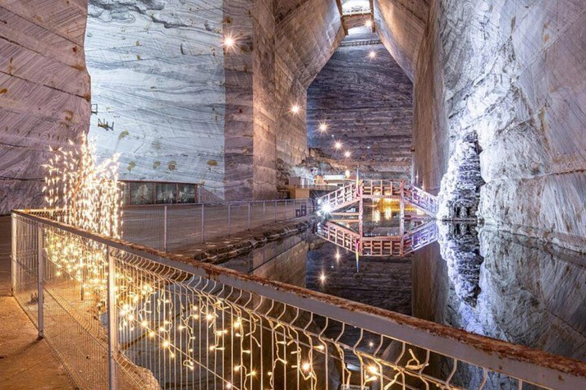 A cave interior with a glass walkway, illuminated by string lights, and a central staircase. 2