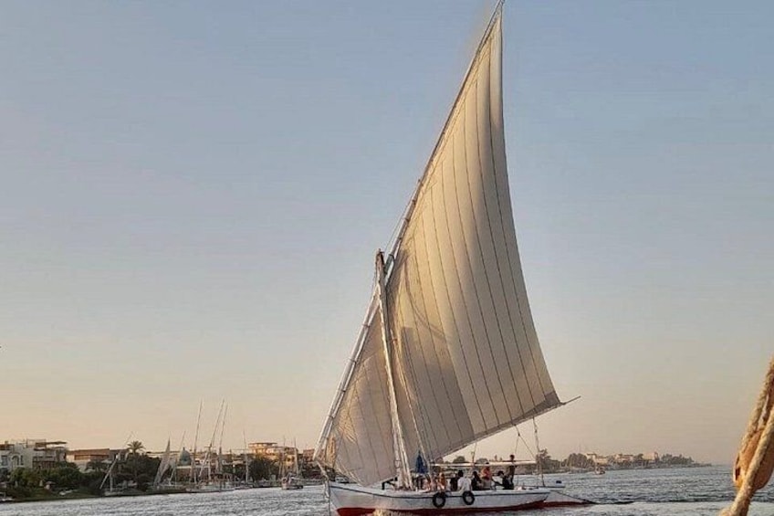 A sailboat with a large sail on the water, a coastline with buildings, and a clear sky. 4