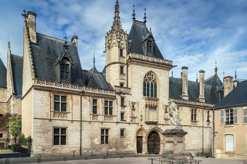 A historic stone building with a large arched entrance, a tall tower with a spire, and a statue in front. 3