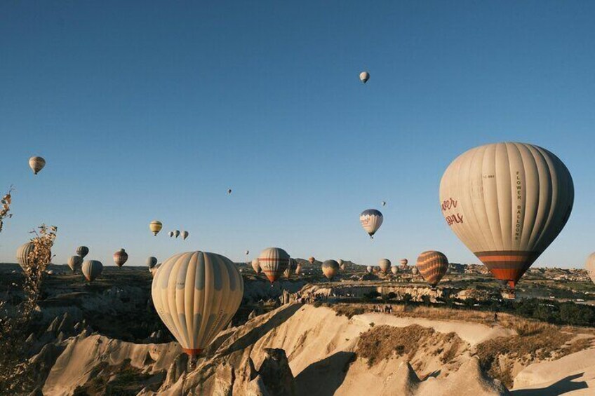 A landscape with multiple hot air balloons in the sky and a rocky terrain below. 4