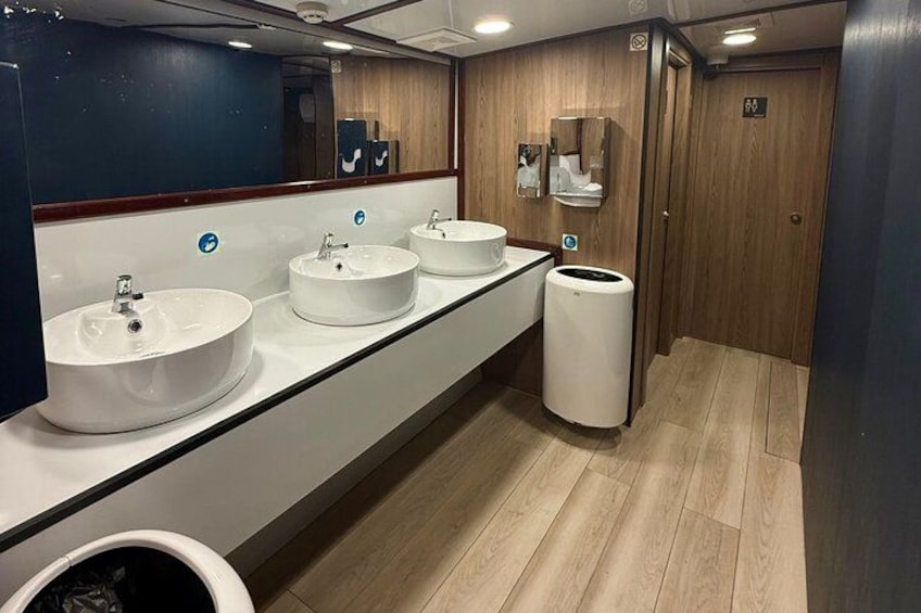 A public restroom with three sinks, a trash can, and a mirror. 3