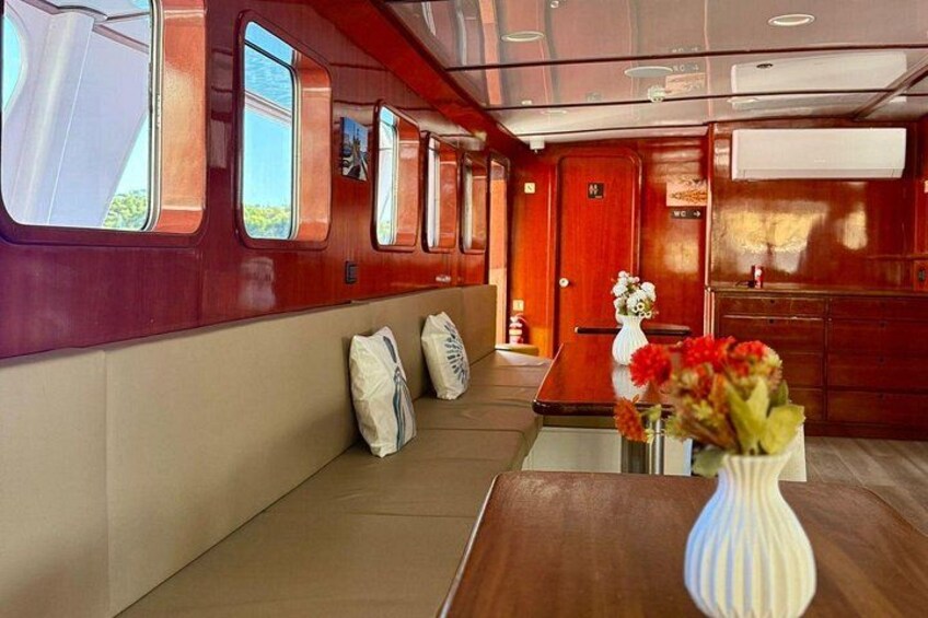 A train interior with wooden paneling, a bench, a table with a vase of flowers, and a door. 2