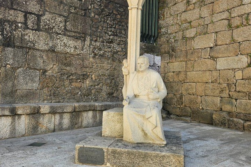A stone statue of a seated figure with a staff, set against a stone wall background. 3