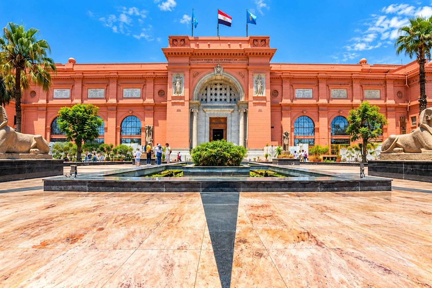 Un edificio grande y ornamentado con una entrada central, palmeras y una fuente al frente. 5