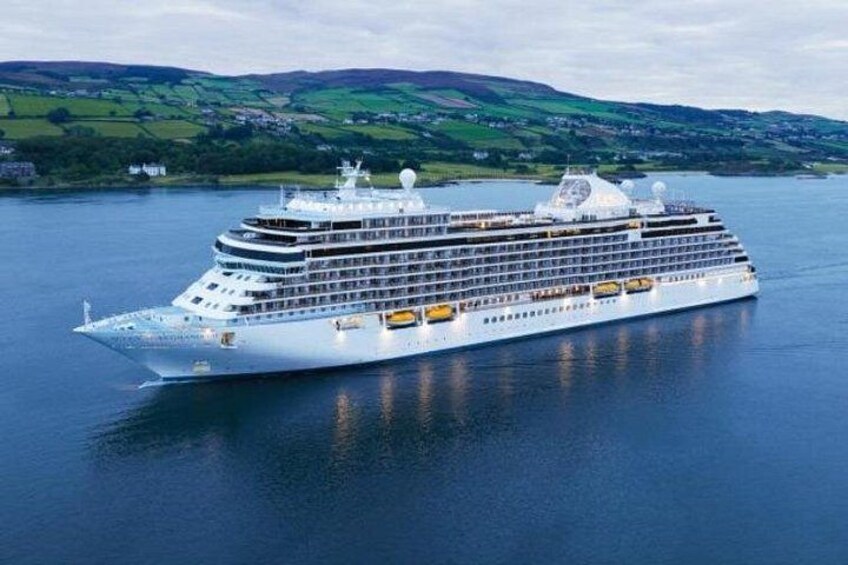 A large cruise ship on calm waters with a hilly landscape in the background. 1