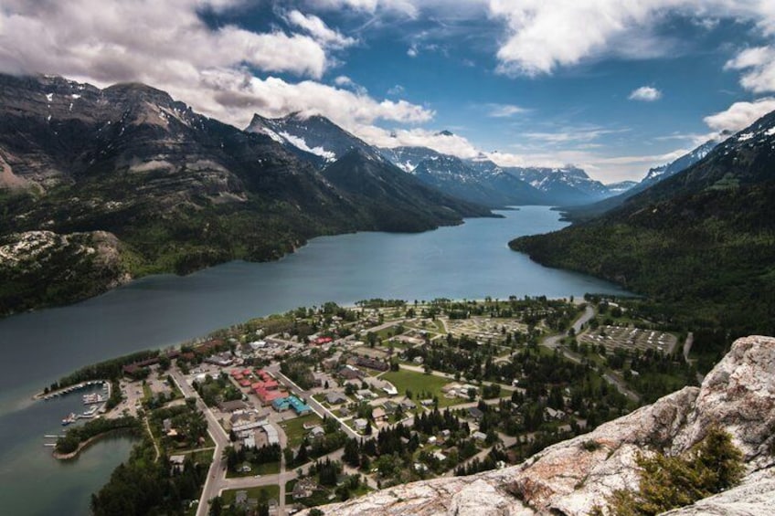 A mountainous landscape with a lake, a town, and snow-capped peaks. 1