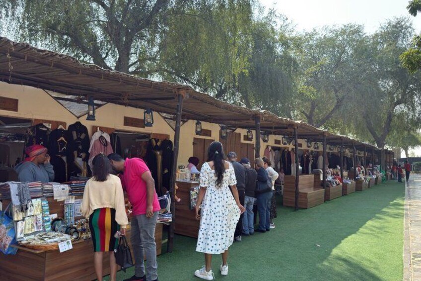 An outdoor market with stalls selling various items, surrounded by trees. 3