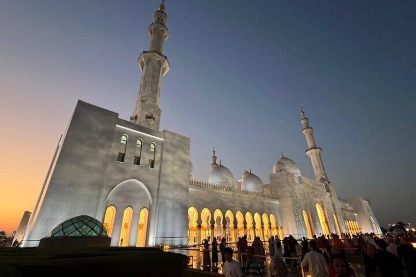 A large mosque with multiple domes and minarets, illuminated at dusk. 1