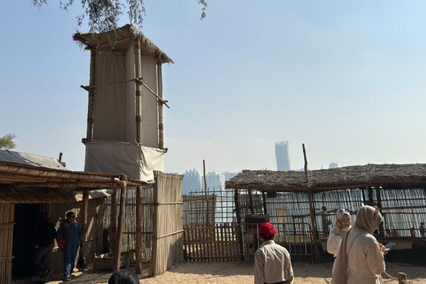 A traditional market with bamboo structures, a water tower, and a distant modern building. 5