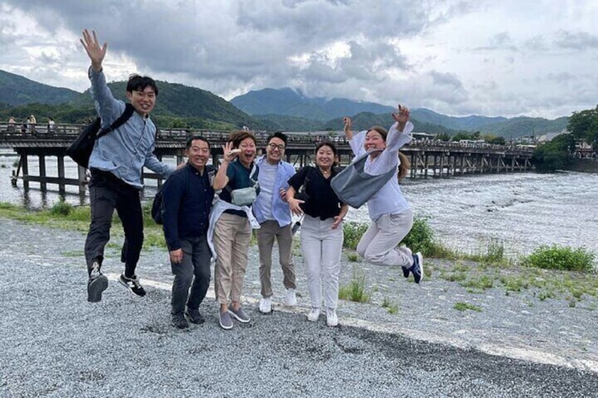 Un groupe de personnes sautant devant une rivière, avec un pont en arrière-plan. 4