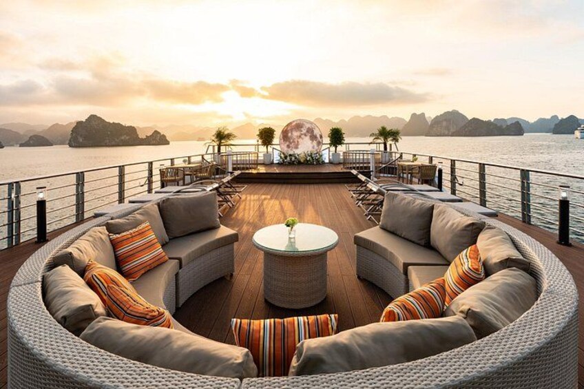 Eine Terrasse mit einer runden Couch, einem runden Tisch und einem Geländer mit Blick auf ein Gewässer und Inseln in der Ferne. 3