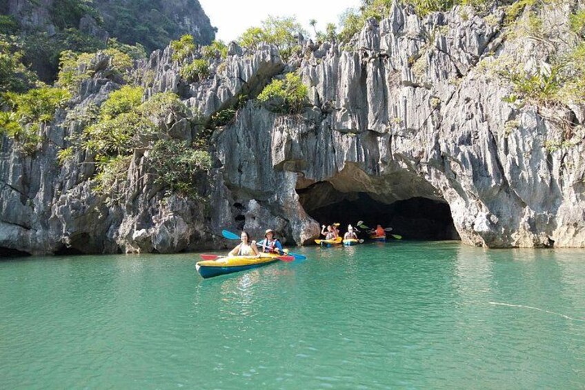A group of people kayaking near a cave entrance surrounded by rocky cliffs. 1