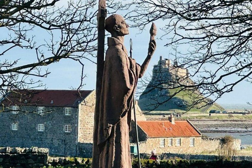 A statue of a person with raised arms, a stone building, and a castle in the background. 1