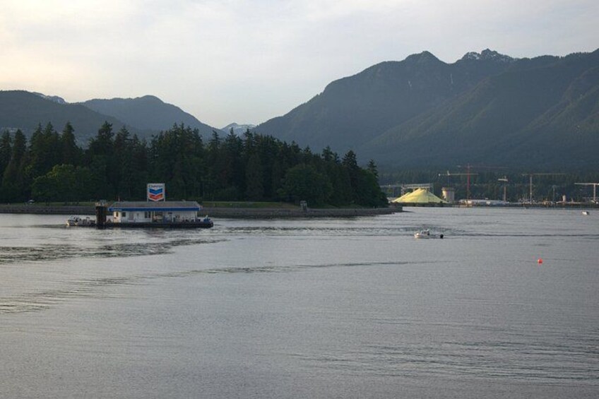 A calm lake with a houseboat, forested hills, and industrial structures in the background. 2