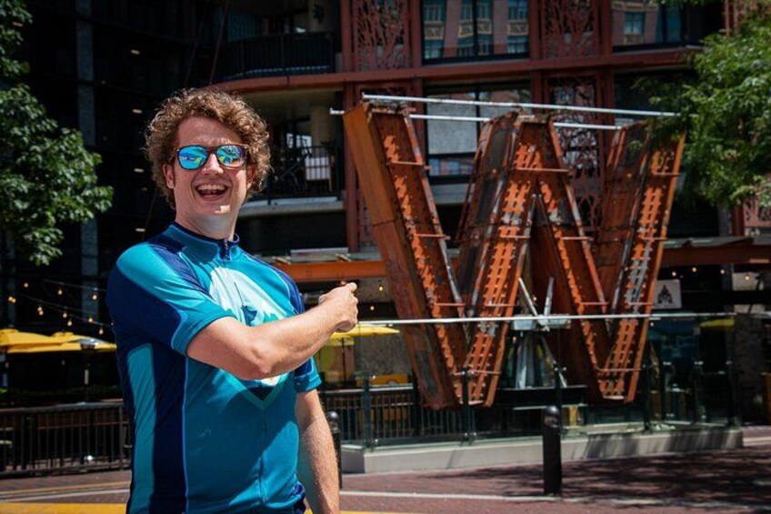 A person in a blue shirt standing in front of a large, rust-colored structure with a distinctive 'W' shape. 4