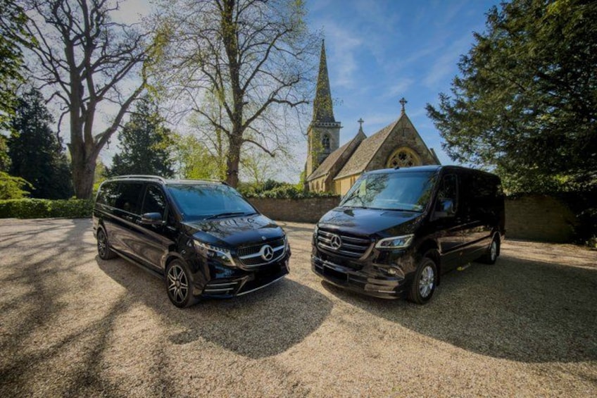 Two black Mercedes-Benz vans parked on a gravel driveway with a church and trees in the background. 5