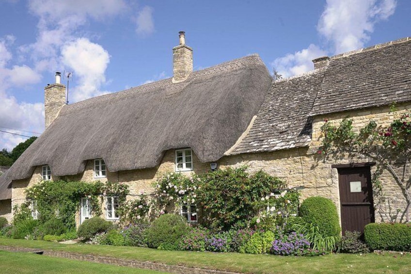 A traditional stone house with a thatched roof, surrounded by lush greenery and flowering plants. 5
