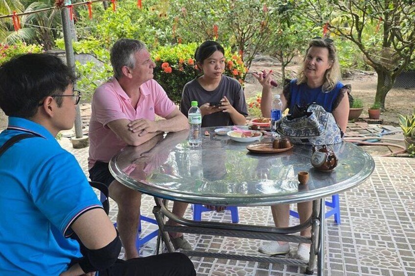 A group of people sitting around a glass table outdoors with a garden in the background. 5