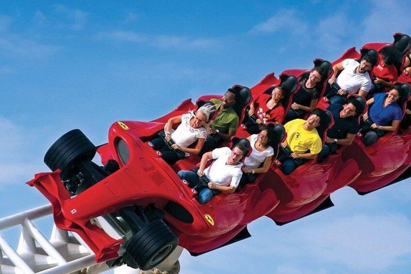 A red roller coaster in motion with passengers seated inside. 4