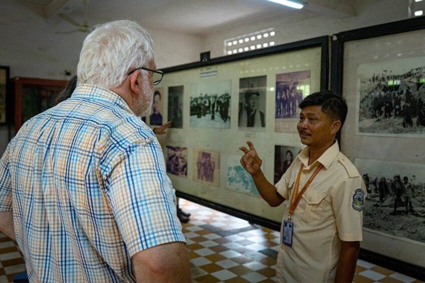 Two individuals in an indoor setting with framed photographs on the wall. 1