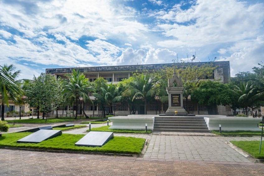 A building with a central monument, surrounded by a landscaped garden with palm trees and a paved pathway leading to the entrance. 2