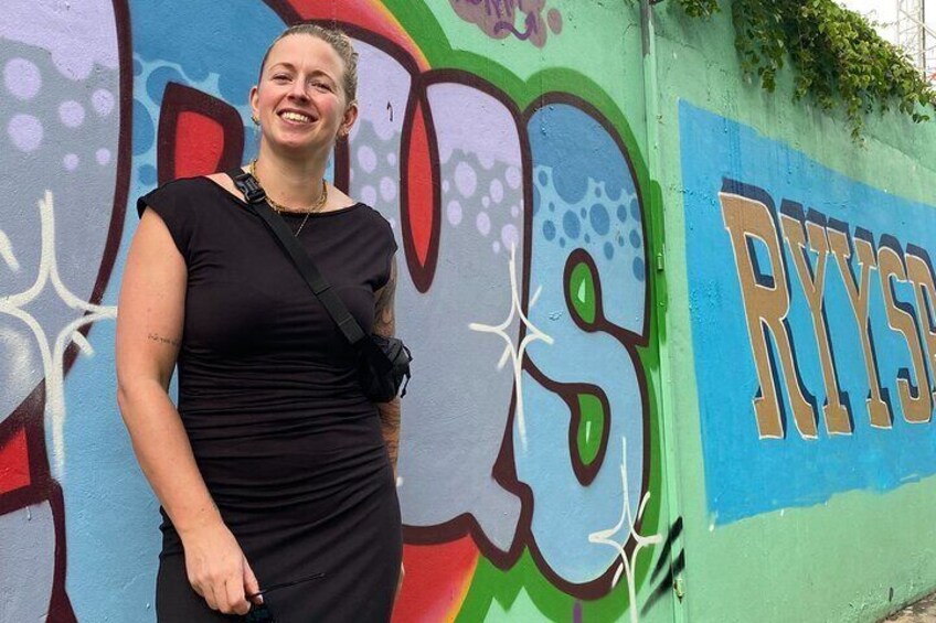 En person står framför en färgglad vägg täckt av graffiti, och bokstäverna ”RYIS” syns tydligt. 2