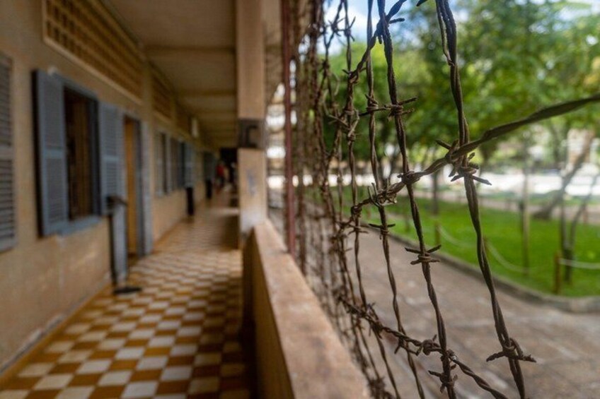 A corridor with a checkered floor, a barred fence, and a building with blue shutters. 4