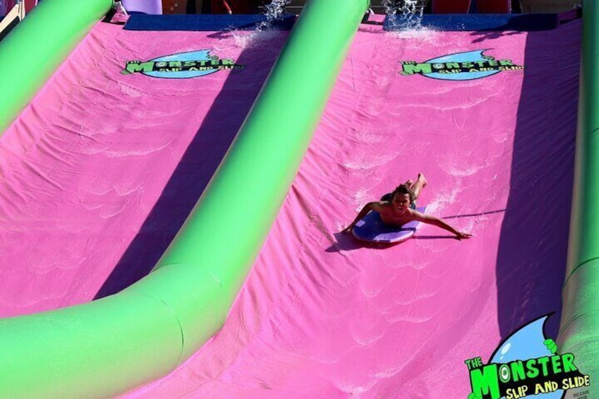 Une personne dévale un toboggan aquatique rose et vert, orné du logo « The Monster ». 2