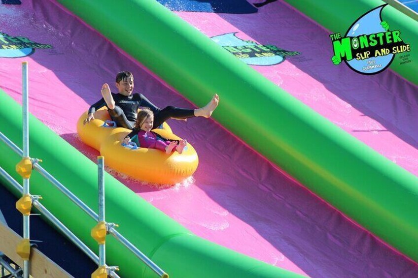 Deux personnes sur une bouée jaune gonflable dévalent une toboggan aquatique vert et rose. 4