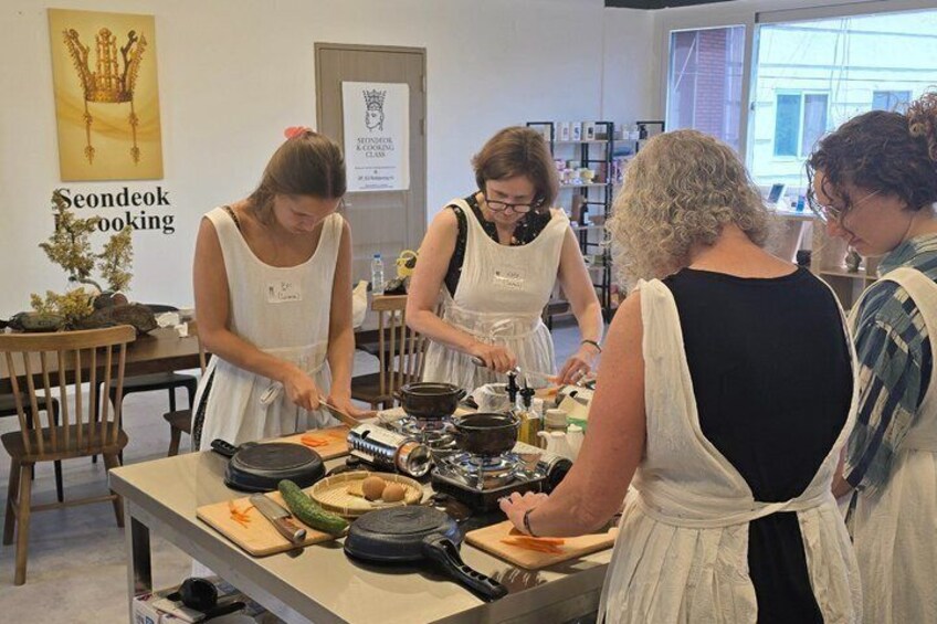 En gruppe mennesker laver mad i et køkken med forskellige ingredienser og redskaber på bordet. 2