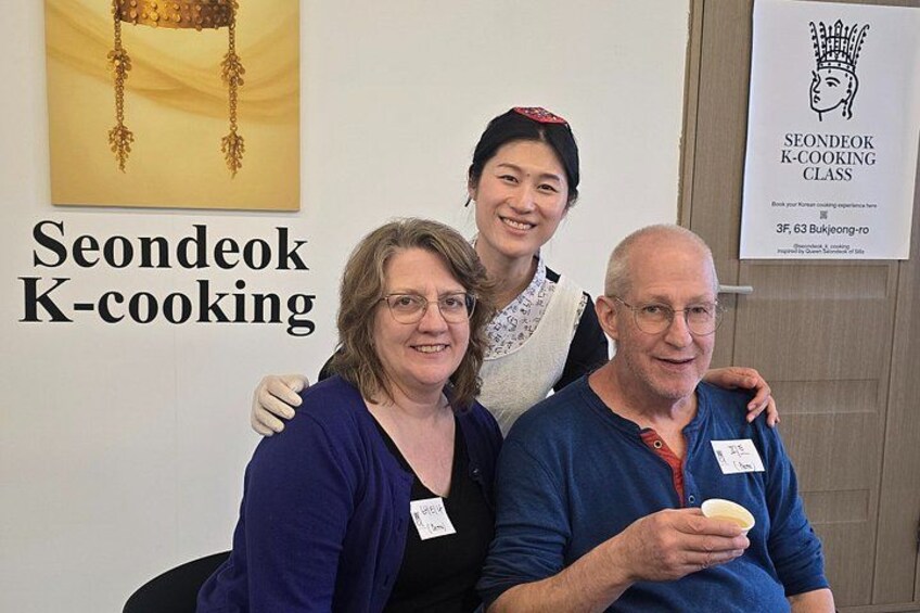 Tre personer sitter i ett rum. På en skylt står det ”Seondeok K-cooking”, och på en annan skylt står det ”Seondeok K-cooking-kurs”. 4