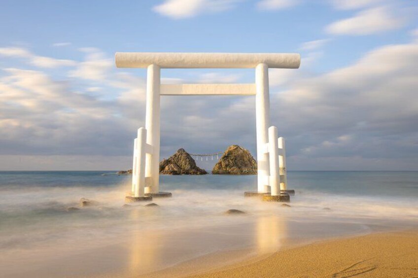 En vit torii-port vid en strand med stilla vatten och en klippig ö i bakgrunden. 5
