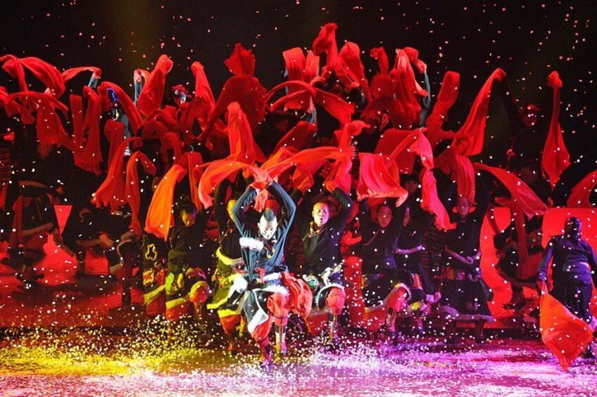 A group of performers in red costumes with a central figure in a blue costume. 1
