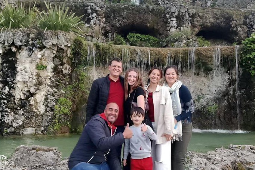 Eine Familie aus sechs Personen posiert vor einem Wasserfall mit felsigem Gelände und viel Grün. 3