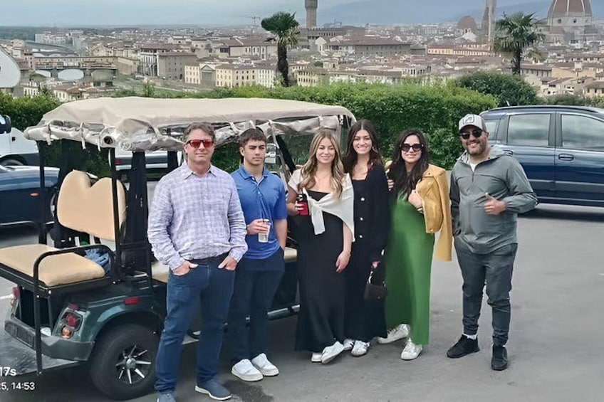 Eine Gruppe von Personen steht vor einem Golfwagen, im Hintergrund ist eine Stadtlandschaft zu sehen. 4