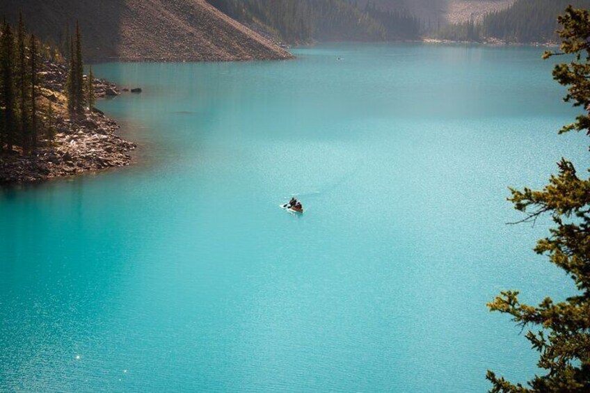 A kayaker on a turquoise lake surrounded by forested mountains. 1