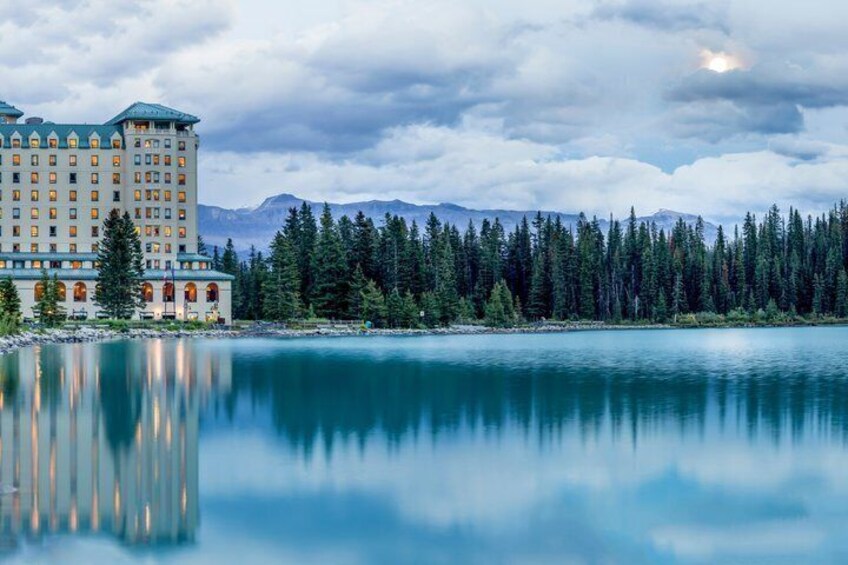 A hotel by a calm lake with mountains in the background. 2