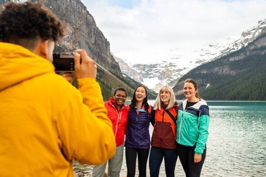 A group of people standing by a lake with mountains in the background. 5