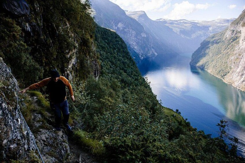 Un excursionista en un sendero montañoso y empinado, con vista a un lago tranquilo rodeado de un bosque denso y terreno accidentado. 1