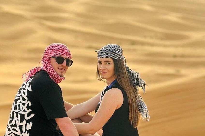 Two people in a desert with sand dunes in the background. 1