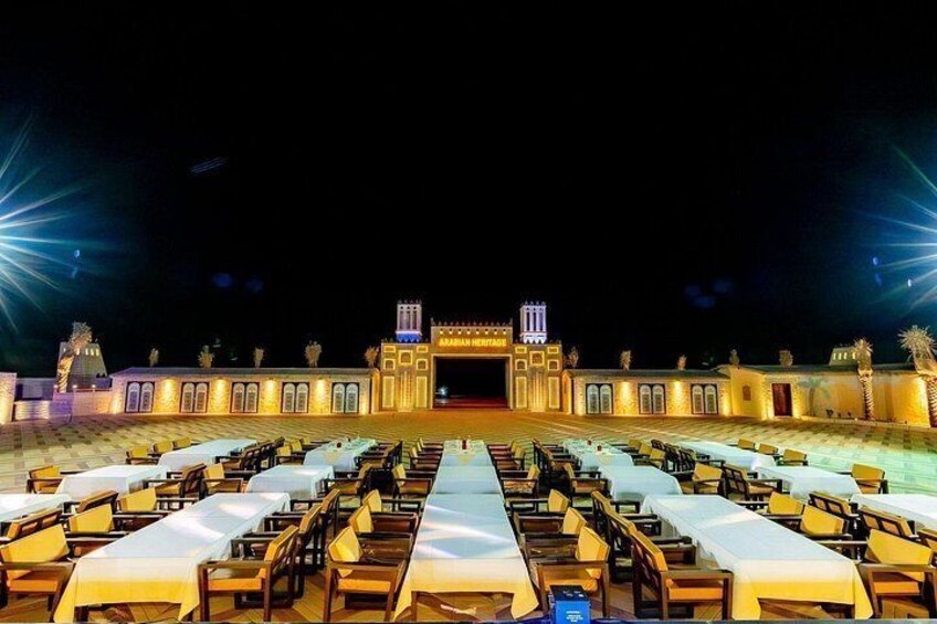 A well-lit outdoor dining area with tables and chairs arranged in rows, leading to a building with a sign that reads 'ARABIAN HERITAGE.' 3