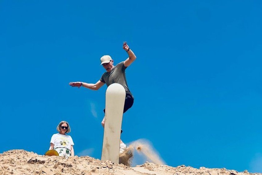 Une personne réalisant une figure sur une planche de snowboard, une autre personne qui regarde, et un ciel bleu dégagé. 5