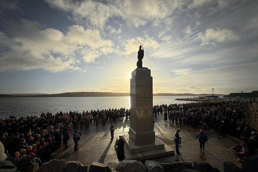 A large crowd gathered around a monument by the waterfront during sunset. 4