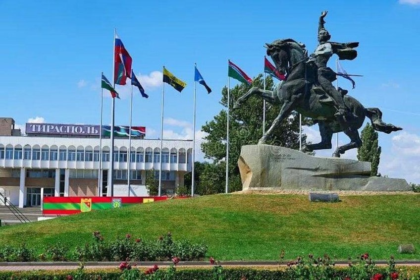 A statue on a hill, a building with flags, and a clear sky. 1