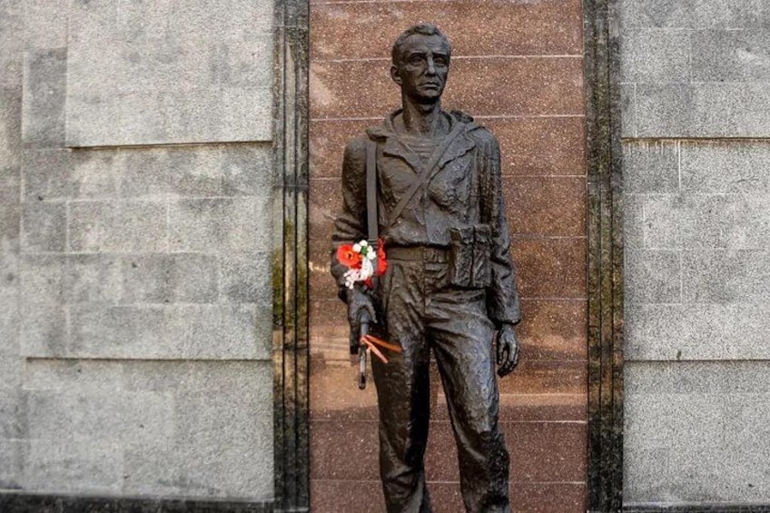 Eine Statue eines Mannes, der einen Blumenstrauß hält, vor einem Steinhaus. 2