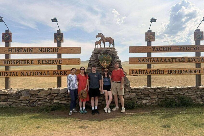 Een groep mensen bij een richtingwijzer met verschillende routes, waaronder Nationaal Park Hustain. 2