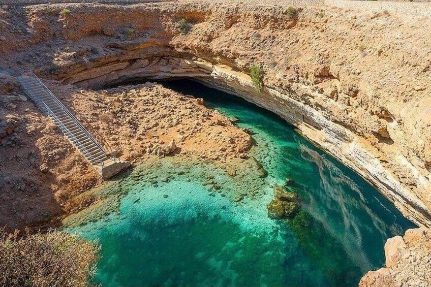 A natural pool with clear turquoise water, a wooden bridge, and rocky terrain. 2